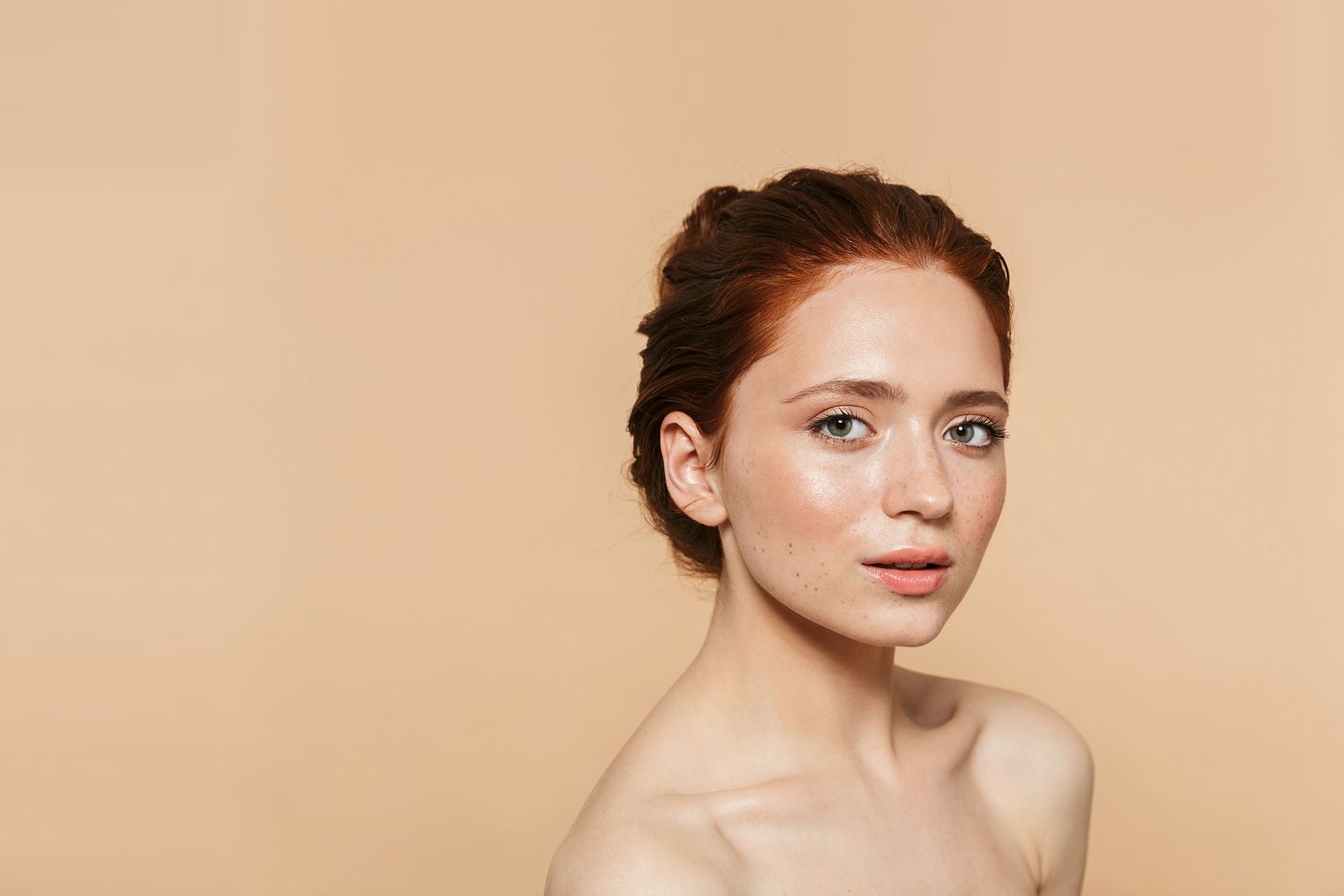A woman with auburn hair pinned up and clear, glowing skin against a warm beige wall