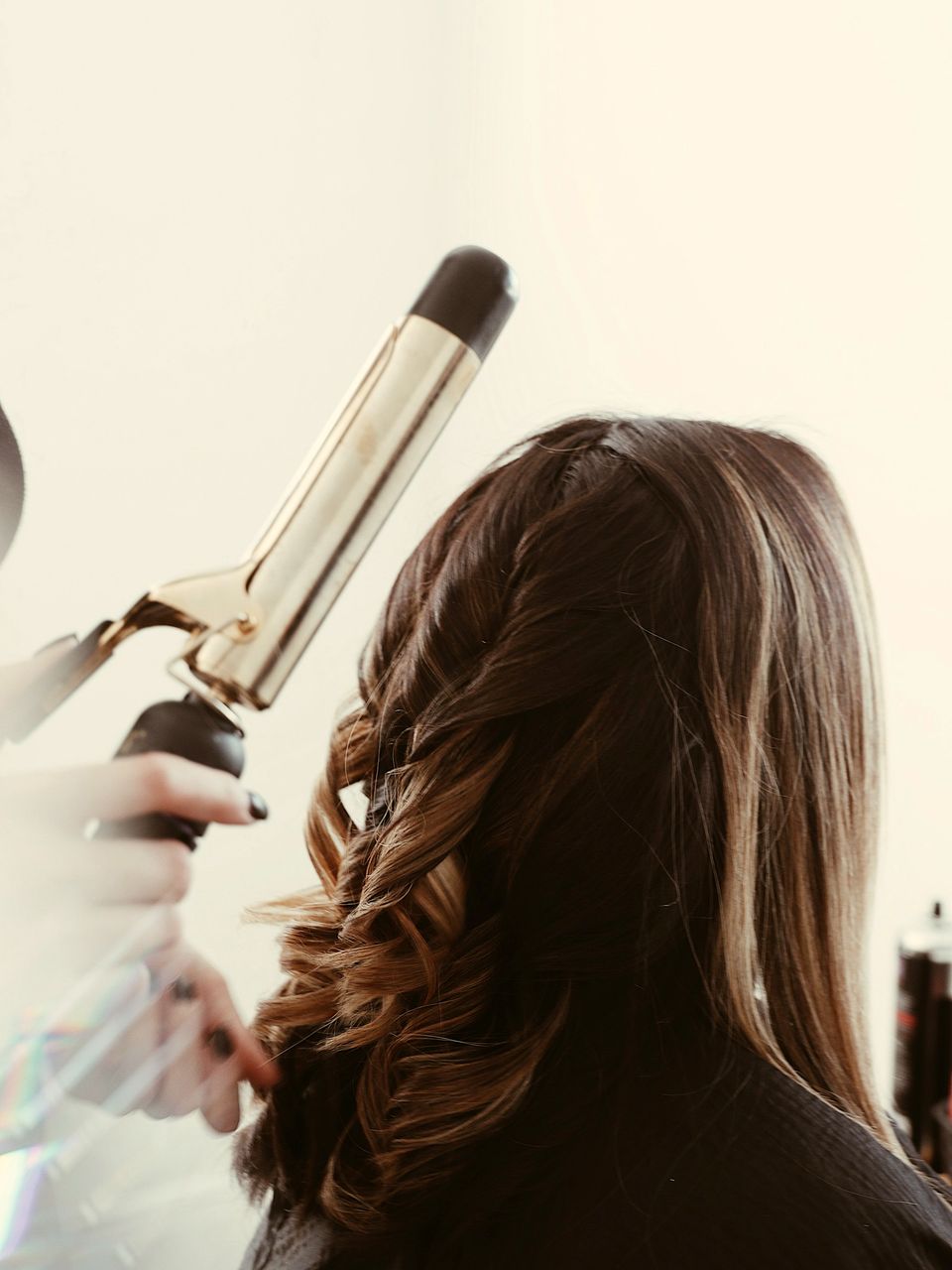 A stylist curling a client’s long brown hair with a tong
