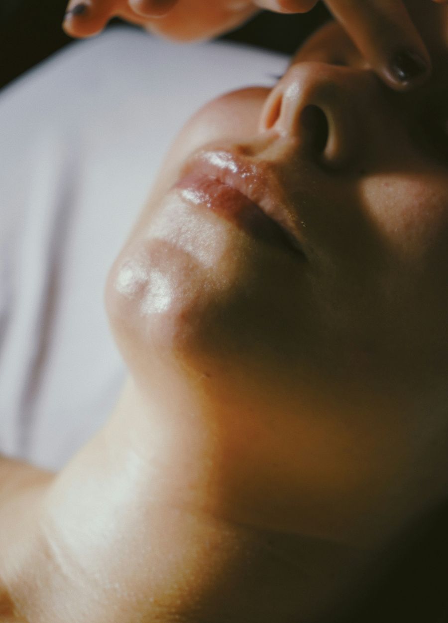 A therapist’s fingertips smoothing a facial treatment over a client’s cheek
